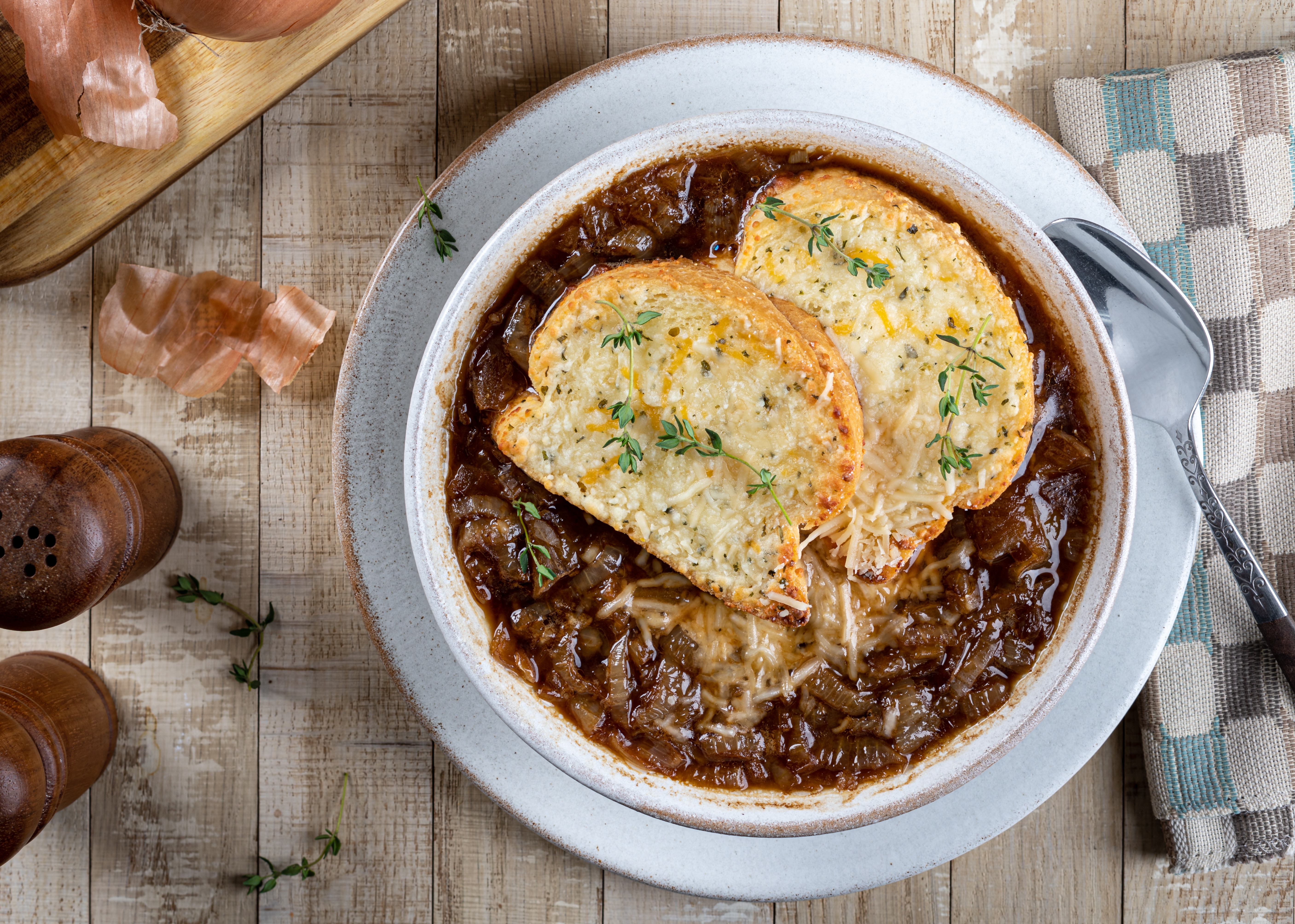 French onion soup with toasted cheese baguette garnished with thyme on a rustic wooden table. | Source: Shutterstock