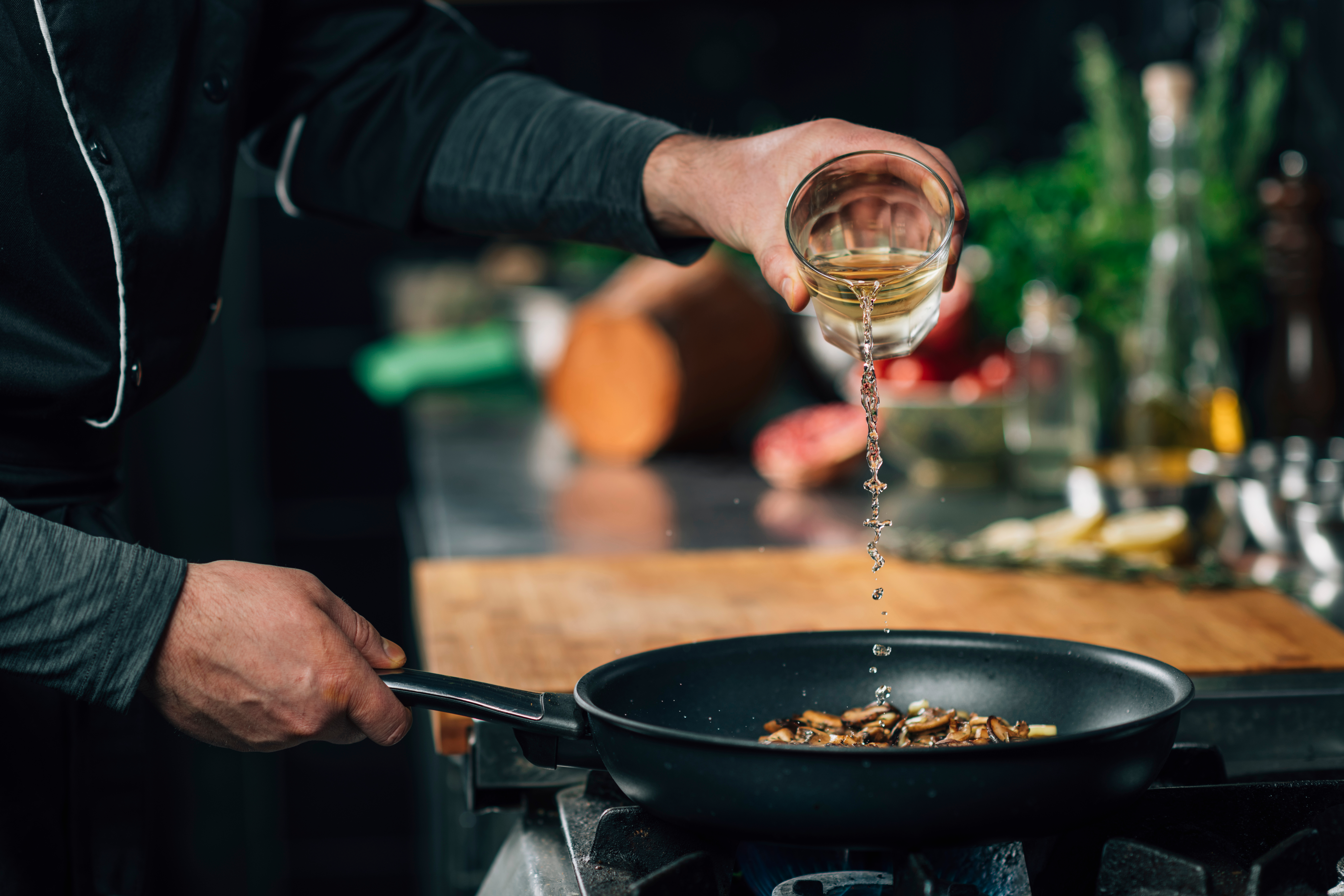 Chef pouring white wine into a sauce pan. | Source: Shutterstock